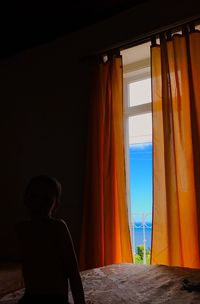 Boy sitting on bed by window