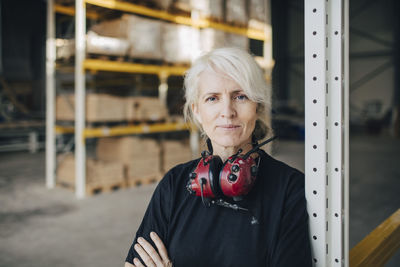 Close-up of smiling worker standing with arms crossed by rack of industry