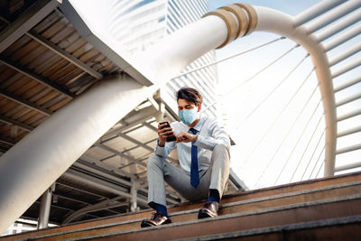 Full length of young man using mobile phone while sitting on staircase