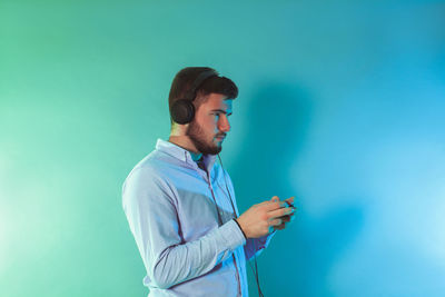 Side view of young man using smart phone against blue background