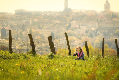 Girl with magnifying glass sitting on grassy field