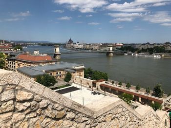 Bridge over river by buildings in city against sky