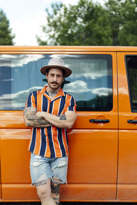 Serious male traveler leaning on van parked in nature and looking at camera during summer adventure
