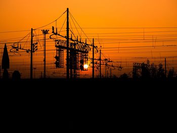 Silhouette electricity pylon against orange sky