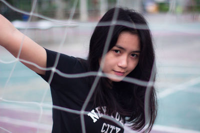 Portrait of young woman on court seen through net