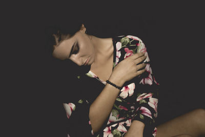 Young woman with eyes closed sitting against black background