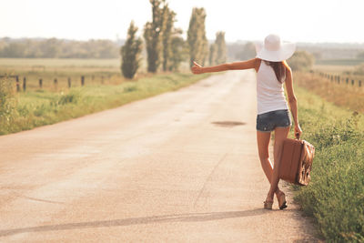 Rear view of woman hitchhiking on road