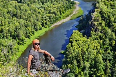 Young man sitting on sunglasses against trees