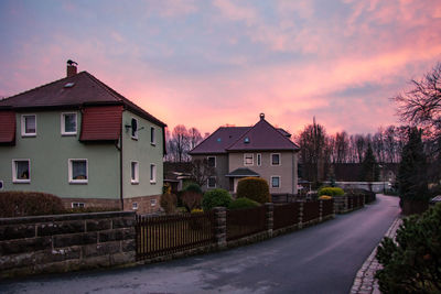 Houses by buildings against sky during sunset