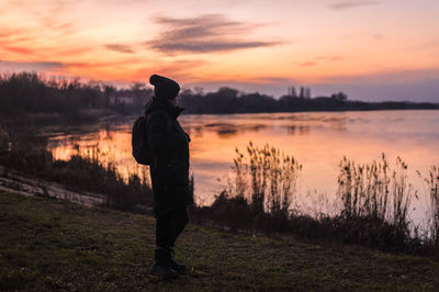 Silhouette of a human on the background of a lake in the forest looking at a beautiful sunset