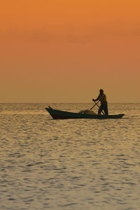 Fisherman oaring boat in sea against orange sky