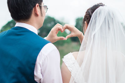 Rear view of couple making heart shape with hands while standing outdoors