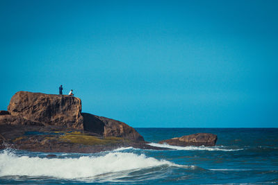 Rock formations by sea against clear blue sky