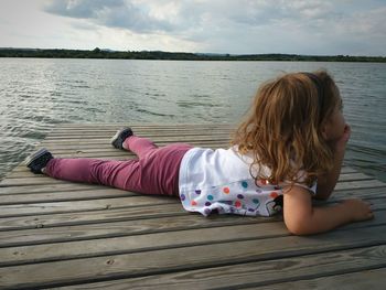 Rear view of girl sitting on lake against sky