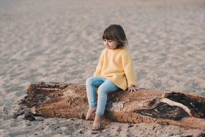 Stylish pretty little child 2-3 year old playing at beach sitting on tree log outdoor. summer season