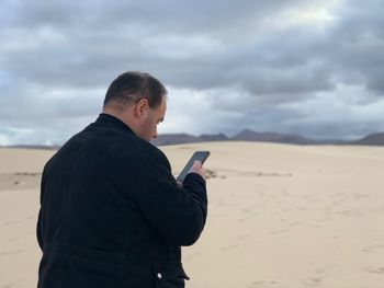 Man using mobile phone at desert against cloudy sky