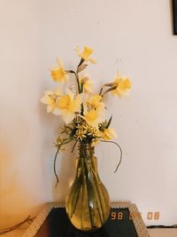 Close-up of yellow flowering plant in vase on table against wall