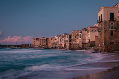 Buildings by sea against blue sky