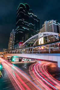 Light trails on road by illuminated buildings in city at night
