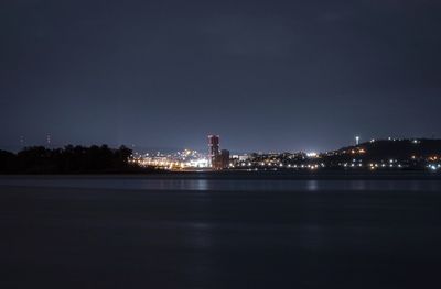 Illuminated buildings by sea against sky at night