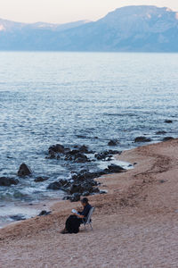 Person reading book while sitting on chair at beach