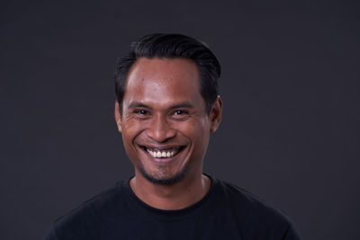 Portrait of smiling young man against black background
