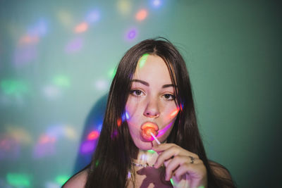 Portrait of young woman eating lollipops against wall