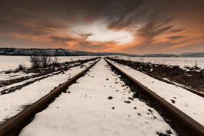 Surface level of snow covered landscape against sky during sunset