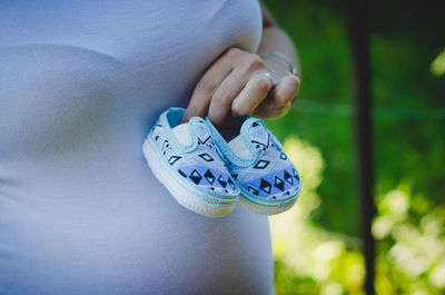 Midsection of pregnant woman holding baby booties over abdomen