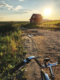 Bicycle parked on field by road against sky