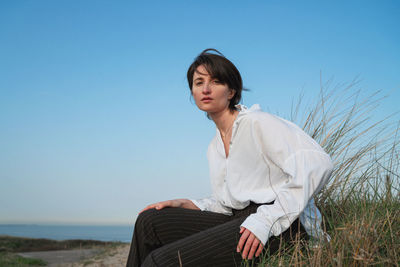 Young woman sitting on land against clear sky