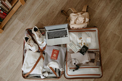 Open baggage with snickers, sweater, laptop, headphones and passport, vintage camera and backpack.