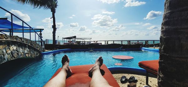 Low section of woman relaxing in swimming pool against sky