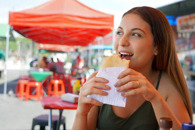 Beautiful young woman eating brazilian traditional food pastel de feira in sao paulo, brazil