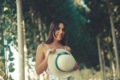 Portrait of smiling young woman standing by trees in forest