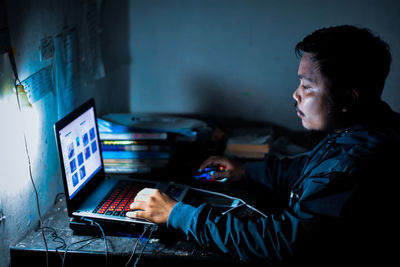 Side view of young man using laptop on desk at home