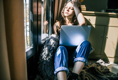 Young girl working at home with laptop next to the window