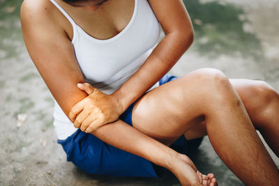 Midsection of woman holding elbow while sitting on road 