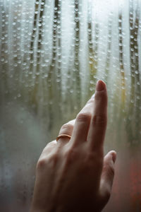 Cropped hand of woman by wet window during rainy season