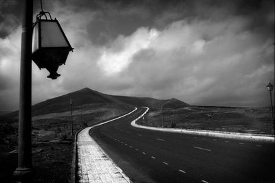 Dramatic view of road amidst arid landscape against cloudy sky in black and white