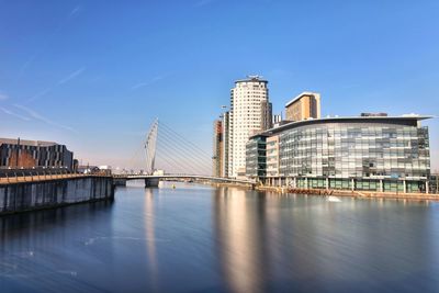 Bridge over river by buildings against blue sky