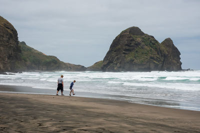 Siblings walking at beach against sky