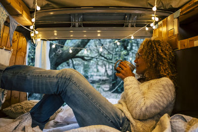 Side view of woman sitting in motor home while holding coffee cup