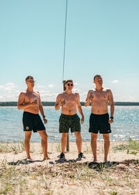 Full length of shirtless man standing on sea shore against sky