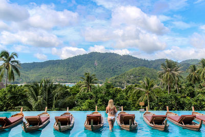 Rear view of woman standing on swimming pool against mountain