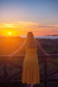 Rear view of woman standing against sky during sunset