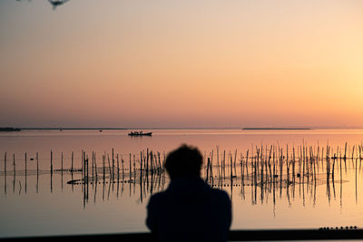 Rear view of silhouette man standing by sea against sky during sunset