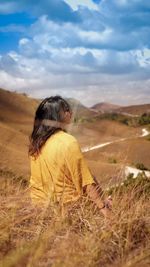 Rear view of woman sitting on field against sky