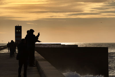 Silhouette people photographing sea against sky during sunset