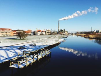 Smoke stack on riverbank emitting smoke against clear blue sky